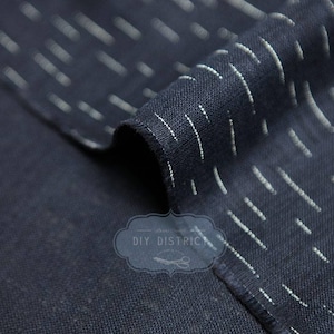 May include: Close-up of a dark blue fabric with white stripes. The fabric is folded over itself, showing the texture of the weave.