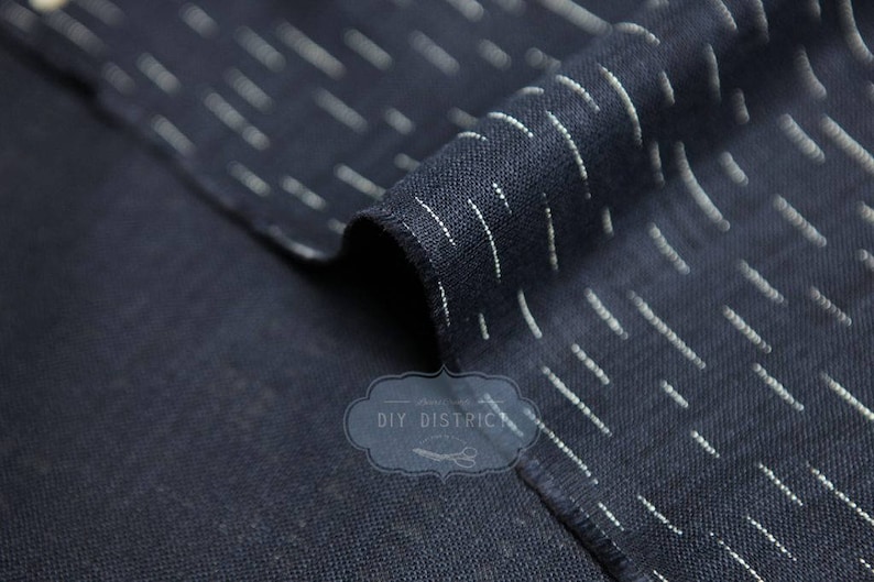 May include: Close-up of a dark blue fabric with white stripes. The fabric is folded over itself, showing the texture of the weave.