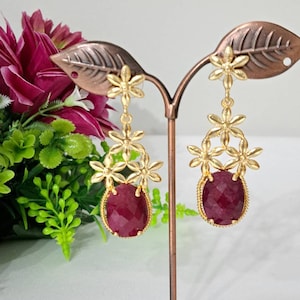 May include: Gold dangle earrings with a red gemstone and a floral design.