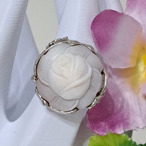 May include: A silver ring with a carved white rose design. The rose is set in a silver ring with a delicate floral design.