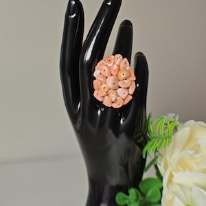 May include: A large statement ring made of pink coral. The ring is set on a black ring holder.