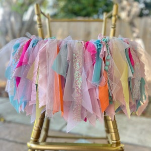 May include: A colorful tulle and ribbon garland with sequins, perfect for a birthday party or special event. The garland is draped over a gold chair.