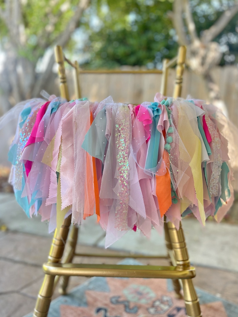 May include: A colorful tulle and ribbon garland with sequins, perfect for a birthday party or special event. The garland is draped over a gold chair.
