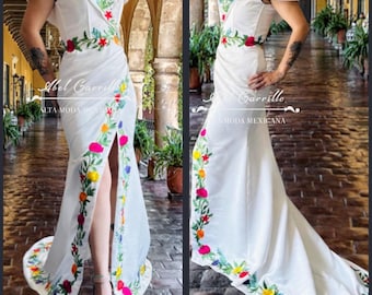 May include: A white off-the-shoulder gown with a long train and a thigh-high slit. The gown is decorated with colorful embroidered flowers. The text "Abel Carrillo Alta Moda" is visible on the left side of the image and "Carrillo Moda Mexicana" is visible on the right side of the image.
