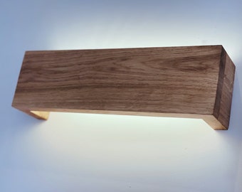 May include: A rectangular wooden wall sconce with a warm, natural wood finish. The sconce has a built-in light source that illuminates the wall behind it.
