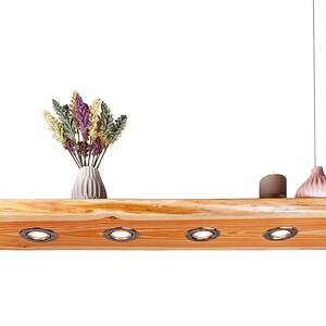 May include: A wooden ceiling light fixture with four integrated spotlights. The fixture is suspended from the ceiling by two cords. The fixture is made of natural wood with a rustic finish. The fixture is decorated with a vase of dried flowers and two decorative ceramic objects.