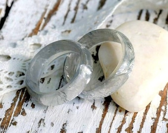 Könnte beinhalten: Zwei silberne Ringe mit einem weißen Stein auf einem weißen Holzgrund mit weißer Spitze.