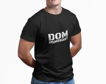 Può includere: Una t-shirt nera a maniche corte con il testo bianco DOM DOMINANT stampato in un audace carattere in stile stencil sul petto. Il capo presenta un girocollo e una vestibilità standard, offrendo un look pulito e semplice per l'uso quotidiano.