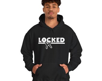 Può includere: Felpa con cappuccio nera con la scritta "LOCKED" in lettere bianche e una grafica a chiave. La felpa ha una tasca frontale e un cappuccio con coulisse. Il modello indossa jeans blu.