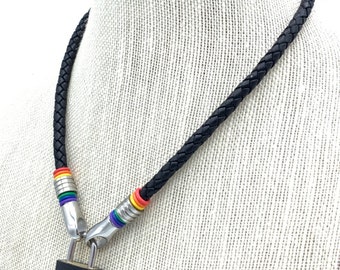 Può includere: Collana in pelle intrecciata nera con un ciondolo a lucchetto nero. La collana presenta dettagli in metallo argentato con perline color arcobaleno. La collana è esposta su un manichino bianco.