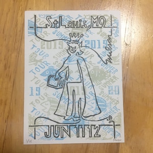 以下が含まれることがあります： 王冠とマントを着た人物の白黒のイラスト。人物は「St. Louis, MO」と「Summer Tour 2019」のテキストのある背景に立っています。「Jun 1112」のテキストは画像の下にあります。