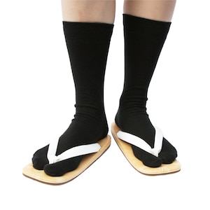 Puede incluir: Un par de calcetines negros con correas blancas sobre sandalias de madera. Las sandalias son de color marr&oacute;n claro.