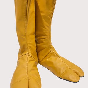 May include: A pair of yellow leather split-toe boots. The boots are tall and have a pointed toe.