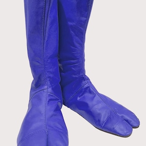 Puede incluir: Un par de botas de cuero azul real vibrante con un diseño distintivo de punta dividida. Estas botas de media caña tienen un acabado liso, detalles de costuras verticales en la parte delantera y una suela plana, con una silueta tipo tabi.