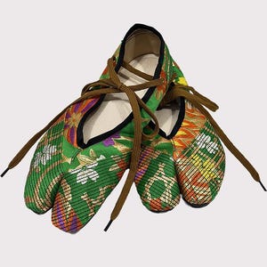 May include: A pair of split-toe shoes featuring a vibrant green fabric with a multi-coloured floral and geometric pattern. The shoes have a black trim along the opening and are secured with brown laces that tie across the top of the foot.