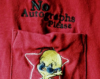 Può includere: Maglietta rossa con una tasca che presenta un uccello giallo ricamato con occhiali da sole e il testo "No Autographs Please".
