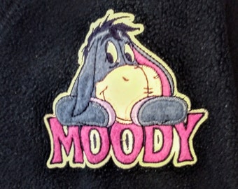 May include: A black fleece jacket with a yellow and pink embroidered patch featuring a cartoon donkey with the word "MOODY" underneath.