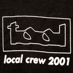 May include: Black t-shirt with a white outline of the band Tool's logo and the text "local crew 2001" in white.