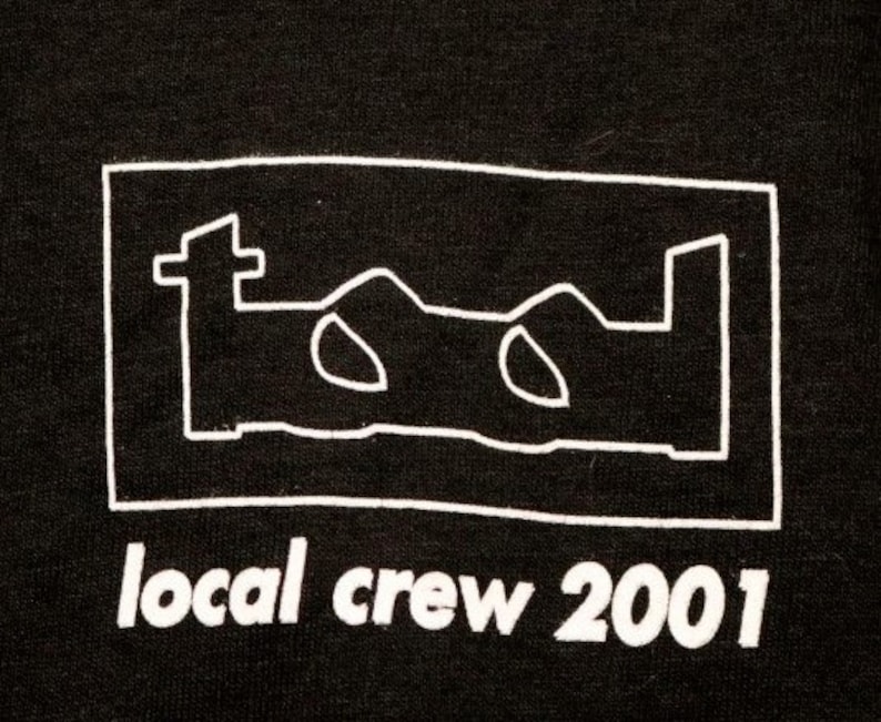 May include: Black t-shirt with a white outline of the band Tool's logo and the text "local crew 2001" in white.