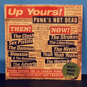May include: A red and yellow sticker with the text "Up Yours!" and "Punk's Not Dead" in large, bold letters. The sticker features a collage of band names from the punk rock genre, including The Clash, Sex Pistols, The Damned, Siouxsie and the Banshees, The Adverts, The Strokes, The Libertines, The Hives, Yeah Yeah Yeahs, The Warlocks, and Punky Pam. The sticker also includes the text "Nasty Green 'Vinyl'" in a green circle.
