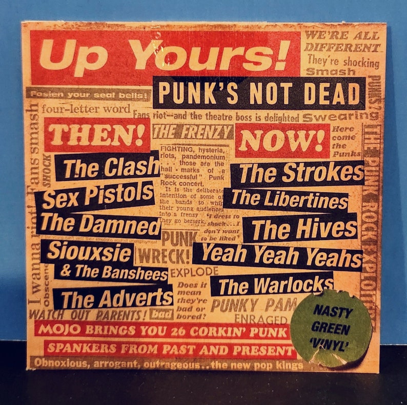 May include: A red and yellow sticker with the text "Up Yours!" and "Punk's Not Dead" in large, bold letters. The sticker features a collage of band names from the punk rock genre, including The Clash, Sex Pistols, The Damned, Siouxsie and the Banshees, The Adverts, The Strokes, The Libertines, The Hives, Yeah Yeah Yeahs, The Warlocks, and Punky Pam. The sticker also includes the text "Nasty Green 'Vinyl'" in a green circle.