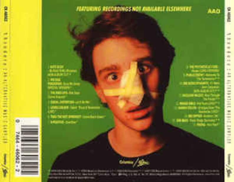 May include: A green CD case with a yellow and green background. The case features a photo of a young man with a yellow bandage over his nose. The text "Featuring recordings not available elsewhere" is printed on the case.