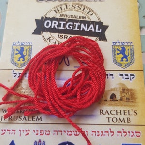 Op de afbeelding: Certificaat voor rode draad met de woorden "Blessed Jerusalem Original" en een zegel met de tekst "ירושלים" in het Hebreeuws. Het certificaat bevat ook een rode draad, een zegel met de tekst "קבר רחל" in het Hebreeuws en de tekst "Rachel's Tomb".