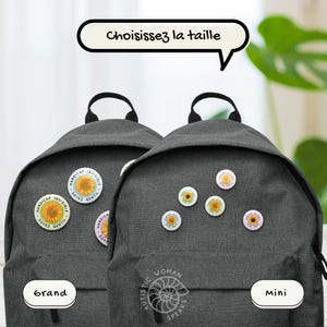 K&ouml;nnte beinhalten: Zwei graue Rucks&auml;cke mit Sonnenblumen-Buttons. Ein Rucksack hat drei Buttons mit dem Text "HANDICAP INVISIBLE SOYEZ GENTIL". Der andere Rucksack hat sechs Sonnenblumen-Buttons. Der Text auf dem Bild lautet "W&auml;hlen Sie die Gr&ouml;&szlig;e".