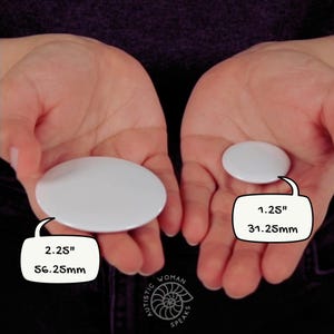 K&ouml;nnte beinhalten: Zwei wei&szlig;e, oval geformte Kn&ouml;pfe werden in offenen H&auml;nden gehalten. Ein Knopf misst 56,25 mm, der andere 31,25 mm. Das Bild enth&auml;lt den Text "AUTISTIC WOMAN SPEAKS".