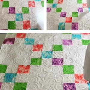 May include: A white quilt with a repeating pattern of colorful squares in red, green, purple, and blue. The quilt has a detailed, swirling quilted design throughout the white background.