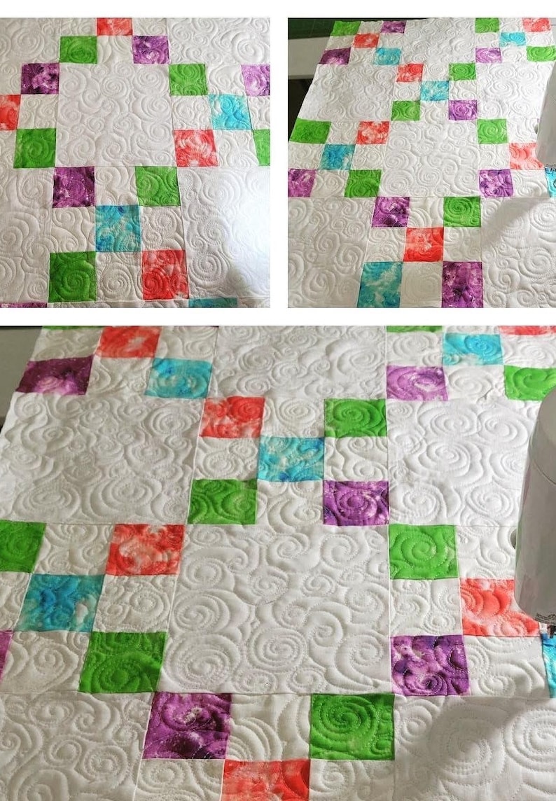 May include: A white quilt with a repeating pattern of colorful squares in red, green, purple, and blue. The quilt has a detailed, swirling quilted design throughout the white background.