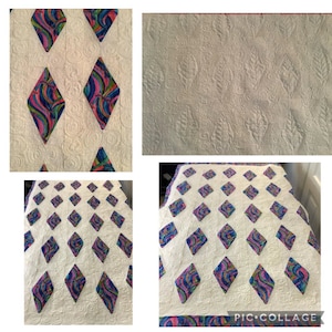 May include: A white quilt with a repeating pattern of colorful diamond shapes. Each diamond is filled with a swirling design of blue, pink, and purple. The quilt has a textured surface with a quilted pattern.
