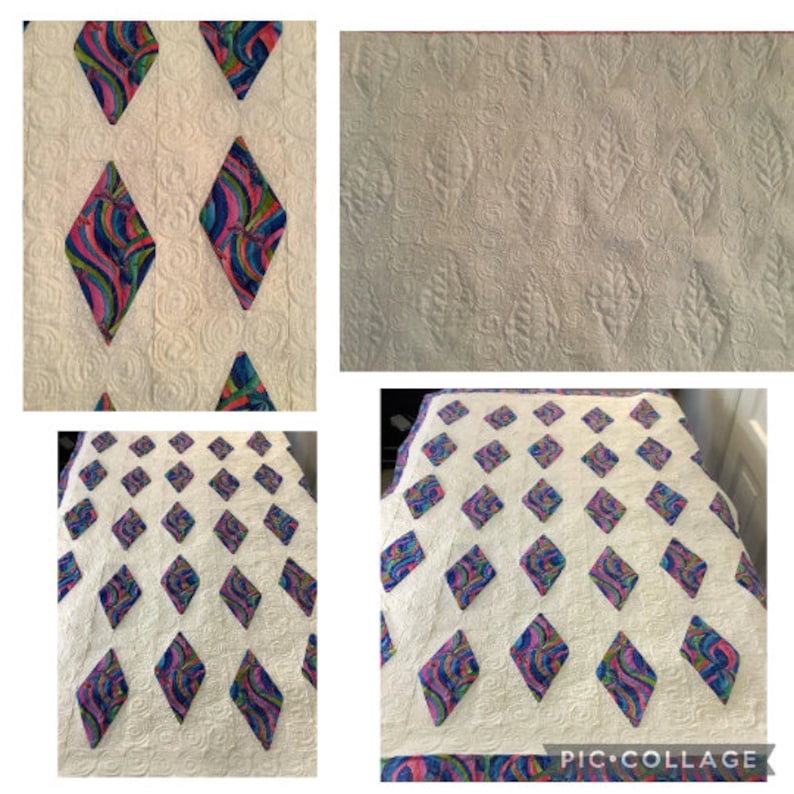 May include: A white quilt with a repeating pattern of colorful diamond shapes. Each diamond is filled with a swirling design of blue, pink, and purple. The quilt has a textured surface with a quilted pattern.