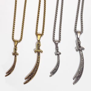 May include: Four necklaces with sword pendants. Two are gold-toned, and two are silver-toned. The pendants have a curved blade design with etched detailing. The chains are a linked style, and the background is white.