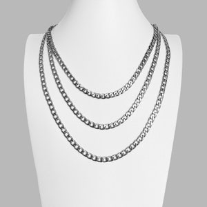 Peut inclure: Trois colliers en chaîne argentés de différentes longueurs et épaisseurs superposés sur un buste de mannequin blanc.