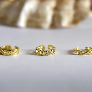 May include: Three gold ear cuffs with different designs. The ear cuffs are on a white surface.