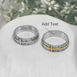 Peut inclure: Deux bagues en argent avec un motif de croix. L'une des bagues porte l'inscription "PROMISE". L'autre bague a une croix dorée. Les bagues sont sur une surface blanche. Le texte "Add Text" est au-dessus d'une des bagues.
