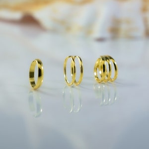 Peut inclure: Trois anneaux en or, une bande simple et deux anneaux empilés, sur une surface blanche.