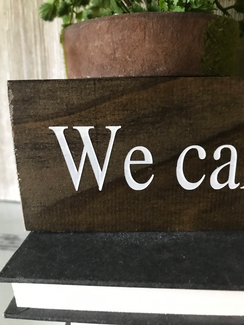 May include: A dark brown wooden sign with white lettering that reads "We can".
