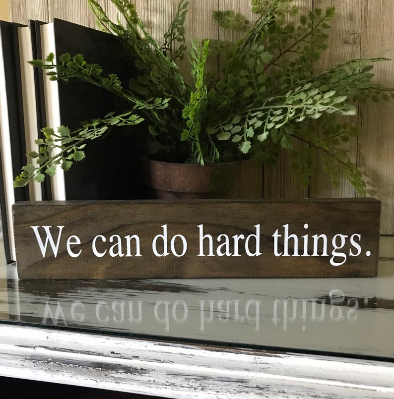 May include: A wooden sign with the text "We can do hard things." in white lettering. The sign is brown and has a rustic look.