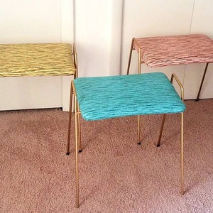May include: Three gold metal stools with different colored fabric seats. The seats are striped in yellow, pink, and teal.