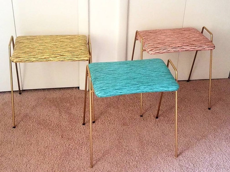 May include: Three gold metal stools with different colored fabric seats. The seats are striped in yellow, pink, and teal.