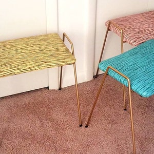 May include: Three gold metal stools with different colored patterned fabric seats. The stools are on a light brown carpet.