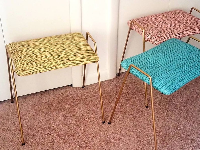 May include: Three gold metal stools with different colored patterned fabric seats. The stools are on a light brown carpet.