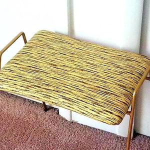 May include: A gold metal bench with a yellow and black striped upholstered seat.
