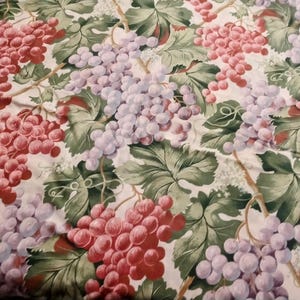 May include: A white fabric with a repeating pattern of green grape vines and bunches of red and purple grapes.
