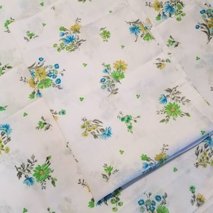 May include: White fabric with a repeating pattern of small blue, yellow, and green floral bouquets. The fabric is folded in thirds.