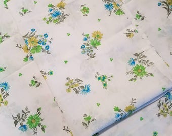 Puede incluir: Tela blanca con un patrón repetitivo de pequeños ramos de flores azules, amarillas y verdes. La tela está doblada en tres.