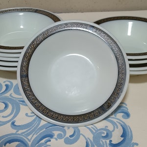 Puede incluir: Un conjunto de cuencos de cerámica blanca con un borde negro y dorado. Los cuencos tienen un patrón decorativo alrededor del borde.