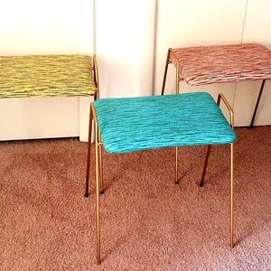 May include: Three gold metal framed stools with different colored patterned fabric upholstery. The stools are on a light brown carpet.